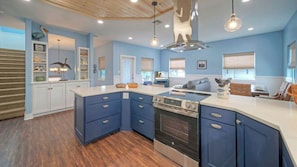 A kitchen with a central island, built-in oven, and a dining area with wicker furniture. - Luxe Coastal Stay w/ Private Pool, Walk to Beach Leave of Absence by Avantstay (Port Aransas)