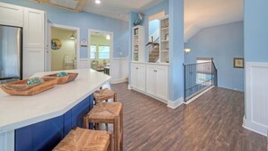 A kitchen with a wooden island, white cabinets, and a staircase leading to a loft area. - Luxe Coastal Stay w/ Private Pool, Walk to Beach Leave of Absence by Avantstay (Port Aransas)