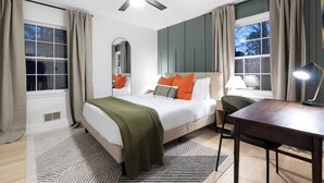 A bedroom with a bed, a desk, a chair, a ceiling fan, and two windows with curtains.