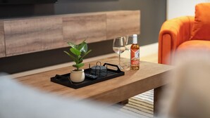 A modern living room with a wooden coffee table, a potted plant, a bottle of liquor, and two glasses.