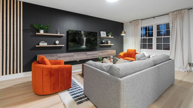 A modern living room with a grey sofa, an orange armchair, a flat-screen TV, and a wooden accent wall.