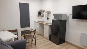 A compact kitchen with a built-in microwave, a refrigerator, a dining table with chairs, and a TV mounted on the wall.