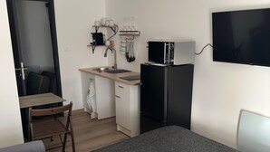 A compact hotel room with a bed, a desk, a kitchenette, and a TV.