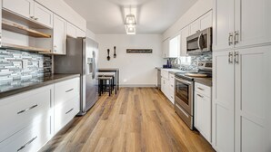 A modern kitchen with white cabinets, stainless steel appliances, and a wooden floor.