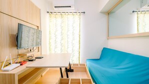 Ein Zimmer mit einem Holztisch, einem blauen Sofa, einem Fernseher und einem Fenster mit Vorhängen.