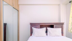 Ein Schlafzimmer mit einem Holz-Kopfteil, zwei weißen Kissen und einem großen Spiegel an der linken Wand.