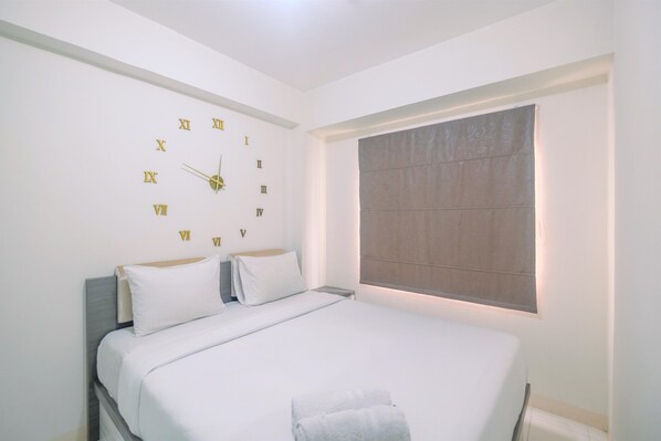 A neatly made bed with white linens, a wall clock, and a window with blinds. - Cozy Living and Relaxing Podomoro Golf View 2BR Apartment (Gunung Putri)