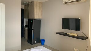 A modern hotel room with a kitchenette, a flat-screen TV mounted on the wall, and a small shelf with a remote control. - Cozy Studio at Belmont Residence Puri Apartment (Jakarta)