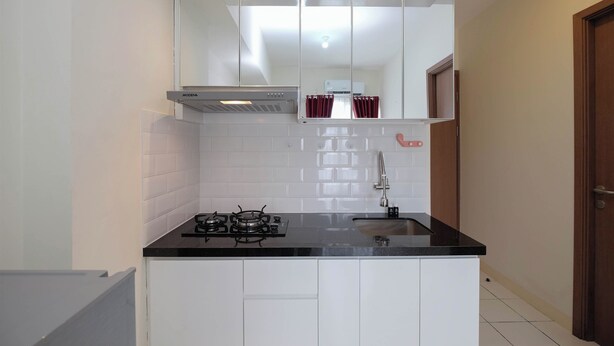 A compact kitchen with white cabinets, a black countertop, a gas stove, and a stainless steel range hood. - Modern Look 2BR at Podomoro Golf View Apartment (Gunung Putri)