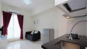 A modern kitchen with a black countertop, stainless steel sink, and a built-in stove. There is a refrigerator and a window with red curtains. - Modern Look 2BR at Podomoro Golf View Apartment (Gunung Putri)