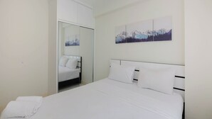 A bedroom with a bed, white bedding, a closet, and a mountain landscape painting on the wall. - Modern Look 2BR at Podomoro Golf View Apartment (Gunung Putri)