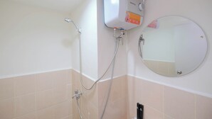 A bathroom with a wall-mounted shower unit, a round mirror, and beige tiled walls. - Modern Look 2BR at Podomoro Golf View Apartment (Gunung Putri)