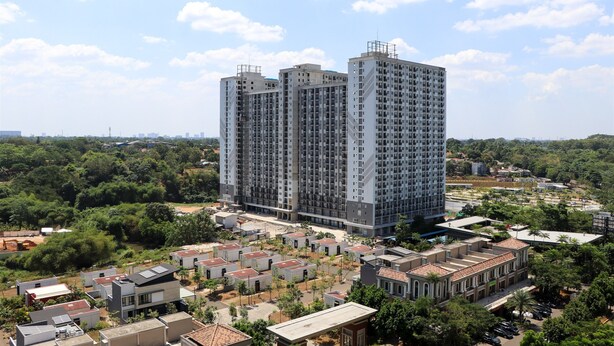 A high-rise residential building with multiple balconies, surrounded by smaller houses and greenery. - Spacious and Good 2BR at Podomoro Golf View Apartment (Gunung Putri)