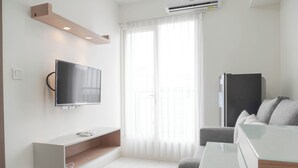 Ein modernes Wohnzimmer mit Fernseher, einer integrierten Regalkonstruktion, einem Glastisch, einem grauen Sofa und einem schwarzen Kühlschrank.