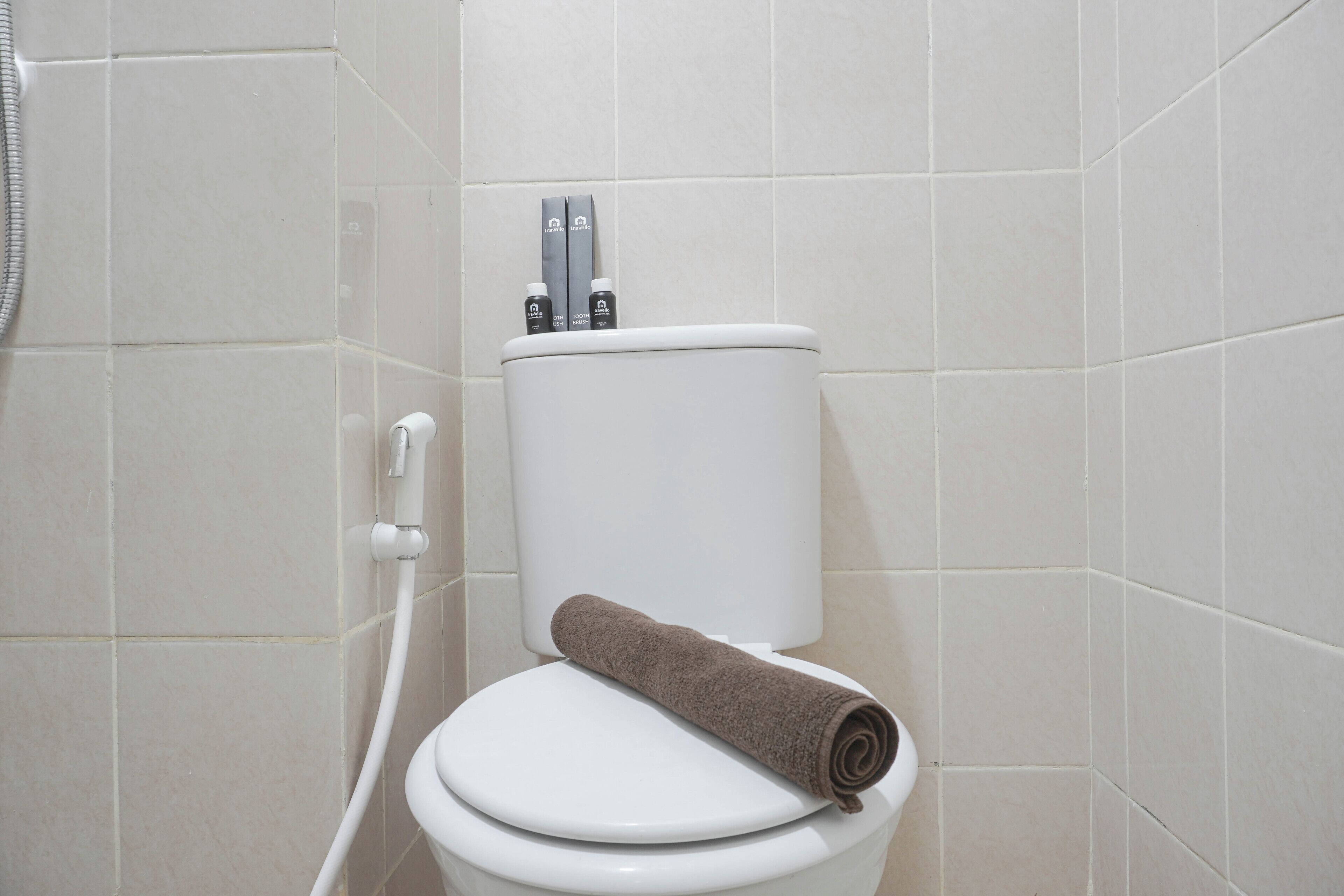 A white toilet with a brown towel on it, a shower hose, and two bottles on the back of the toilet tank.