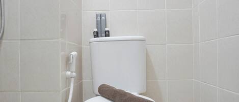 A white toilet with a brown towel on it, a shower hose, and two bottles on the back of the toilet tank.