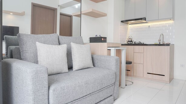 Ein modernes Wohnzimmer mit grauem Sofa, einem kleinen Tisch und einer Küchenzeile mit Holdekor-Schränken und einer weißen Küchenrückwand.
