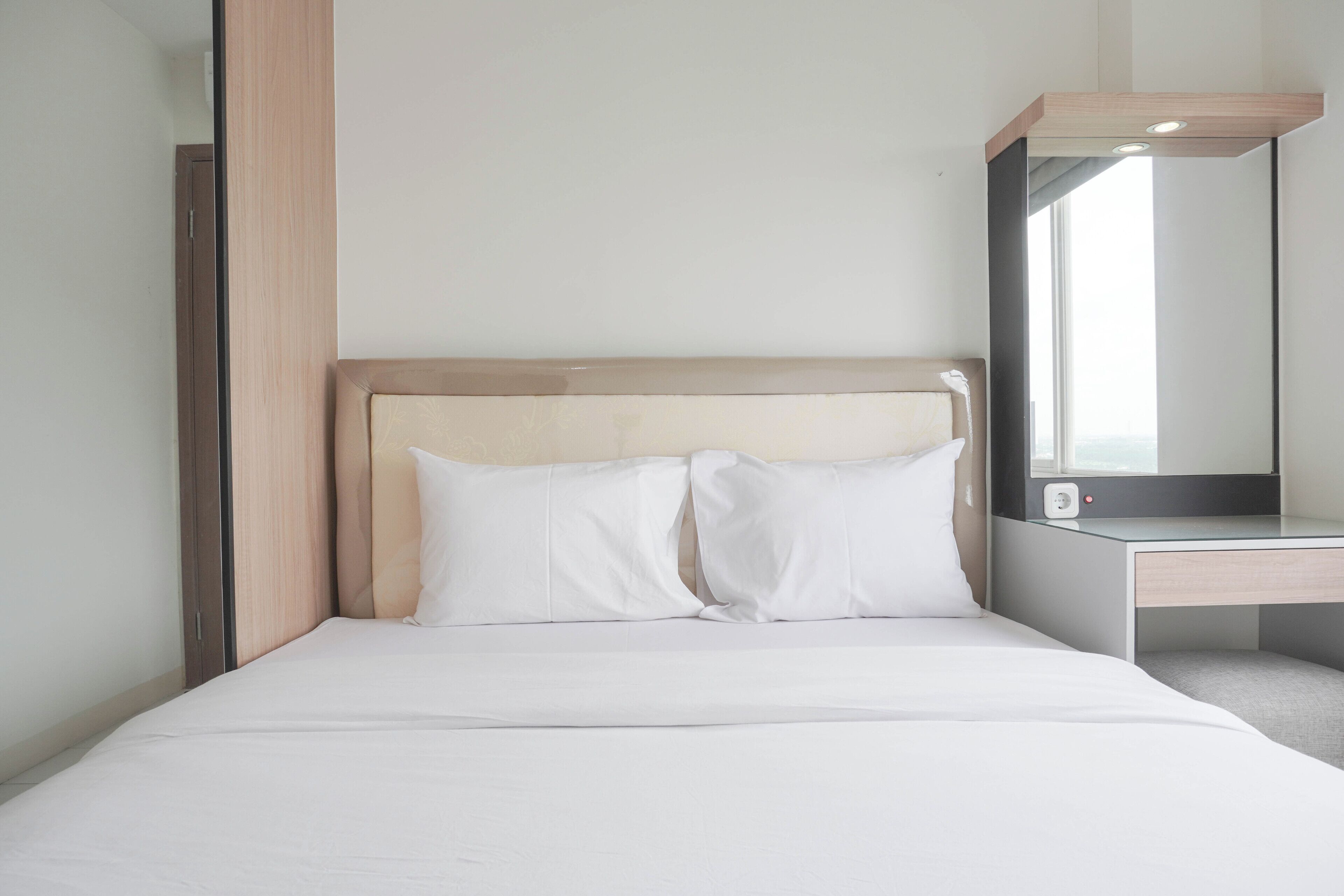 A neatly made bed with white linens and pillows, a wooden headboard, and a bedside table with a mirror.