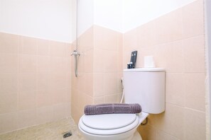 A bathroom with a toilet, a shower, and a towel on the seat. - Well Design 2BR Apartment at Podomoro Golf View (Gunung Putri)
