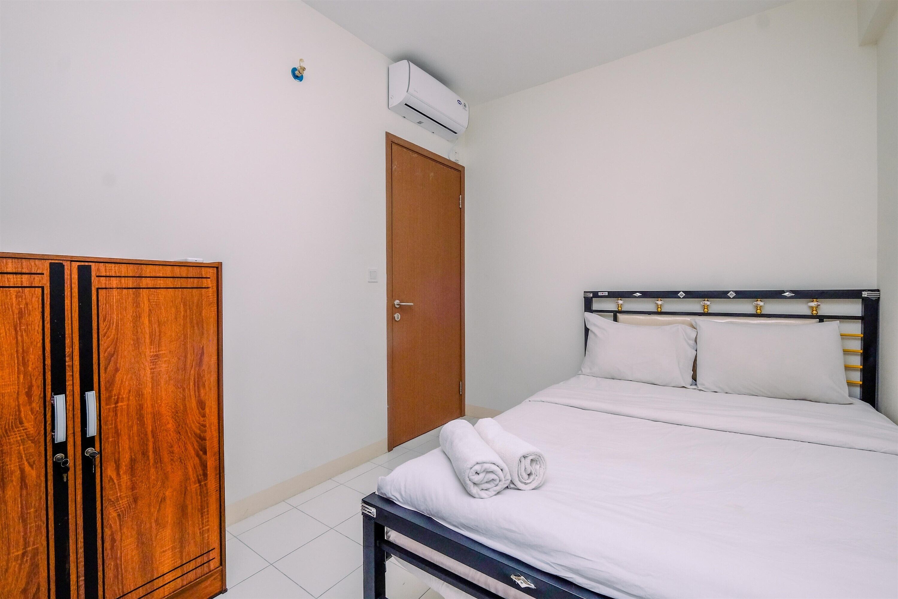 Ein Schlafzimmer mit einem Holzschrank, einem Bett mit weißer Bettwäsche und einer Klimaanlage an der Wand.
