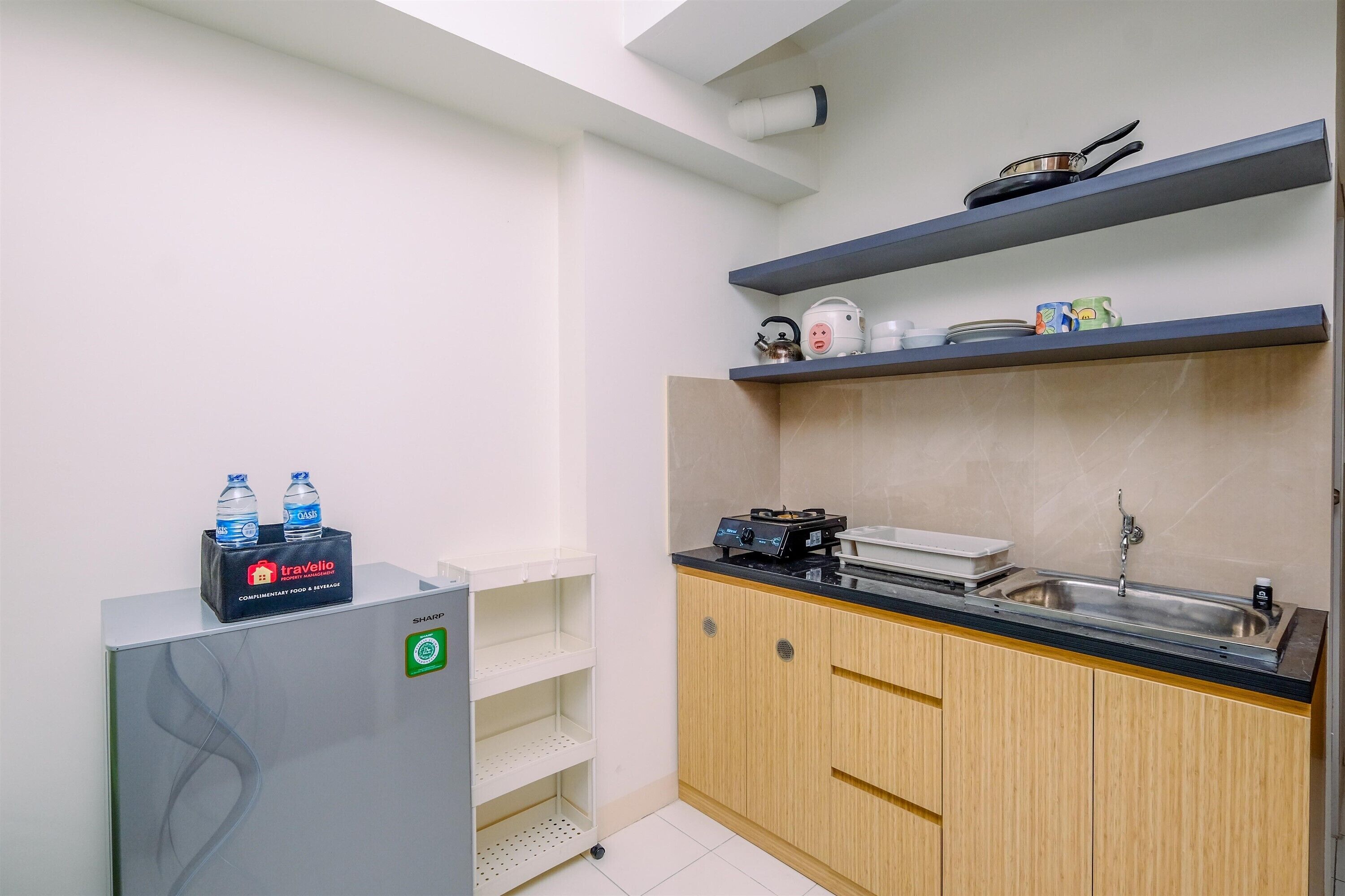 A compact kitchen with a refrigerator, a sink, and a countertop with a kettle and a rice cooker. There are two water bottles on the refrigerator.