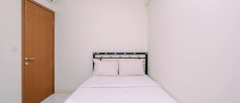 A small, clean room with a bed, a wooden door, and an air conditioning unit on the wall.