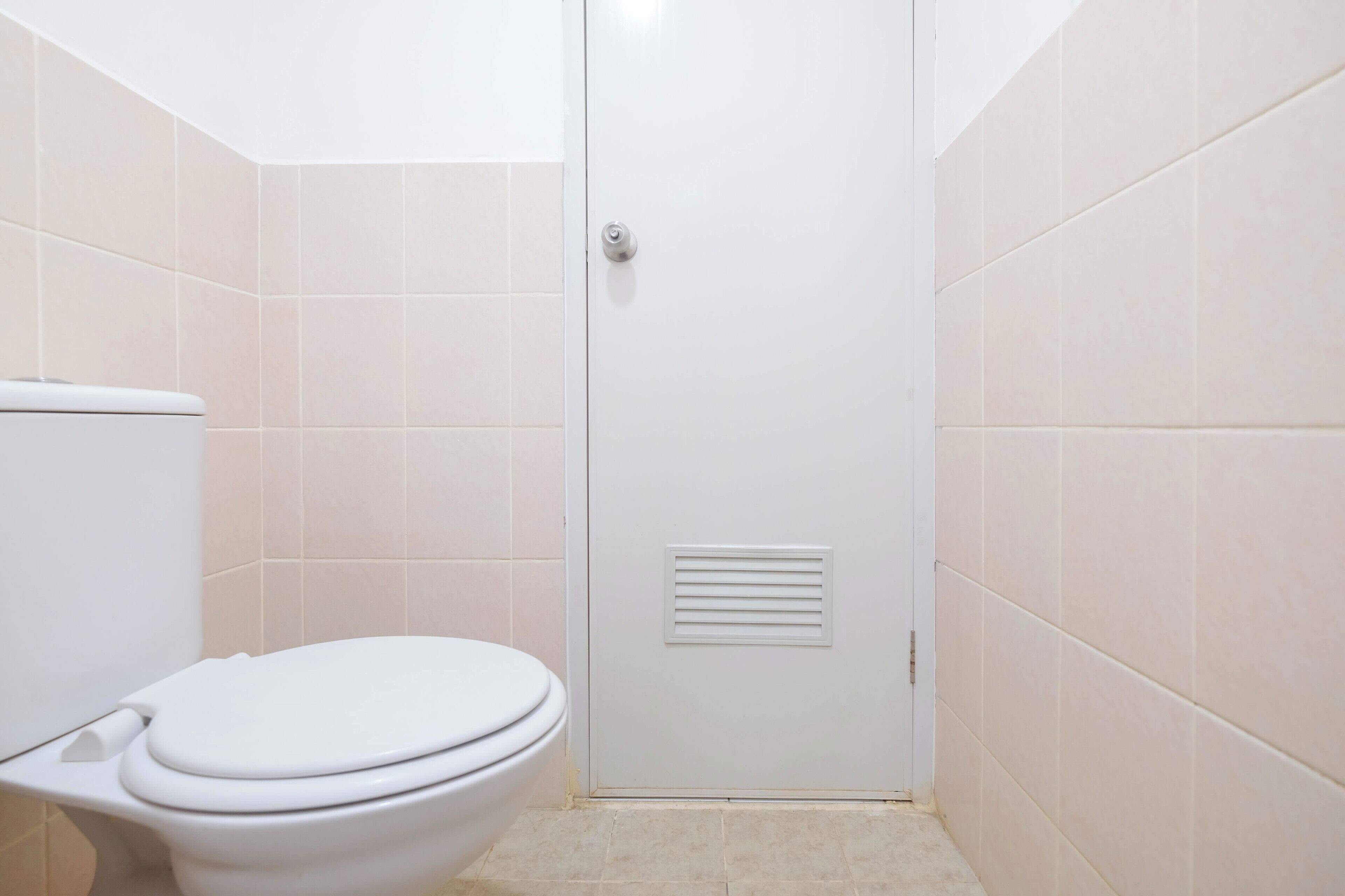 Un bagno con il water, una porta dotata di boccaporto e piastrelle beige su pareti e pavimento.