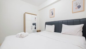 A neatly made bed with white linens, a dark headboard, and two white pillows. A wooden-framed mirror hangs on the wall above the bed.