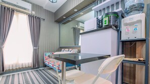 A compact hotel room with a small table, two white chairs, a bed with a colorful blanket, a water dispenser, and a refrigerator.