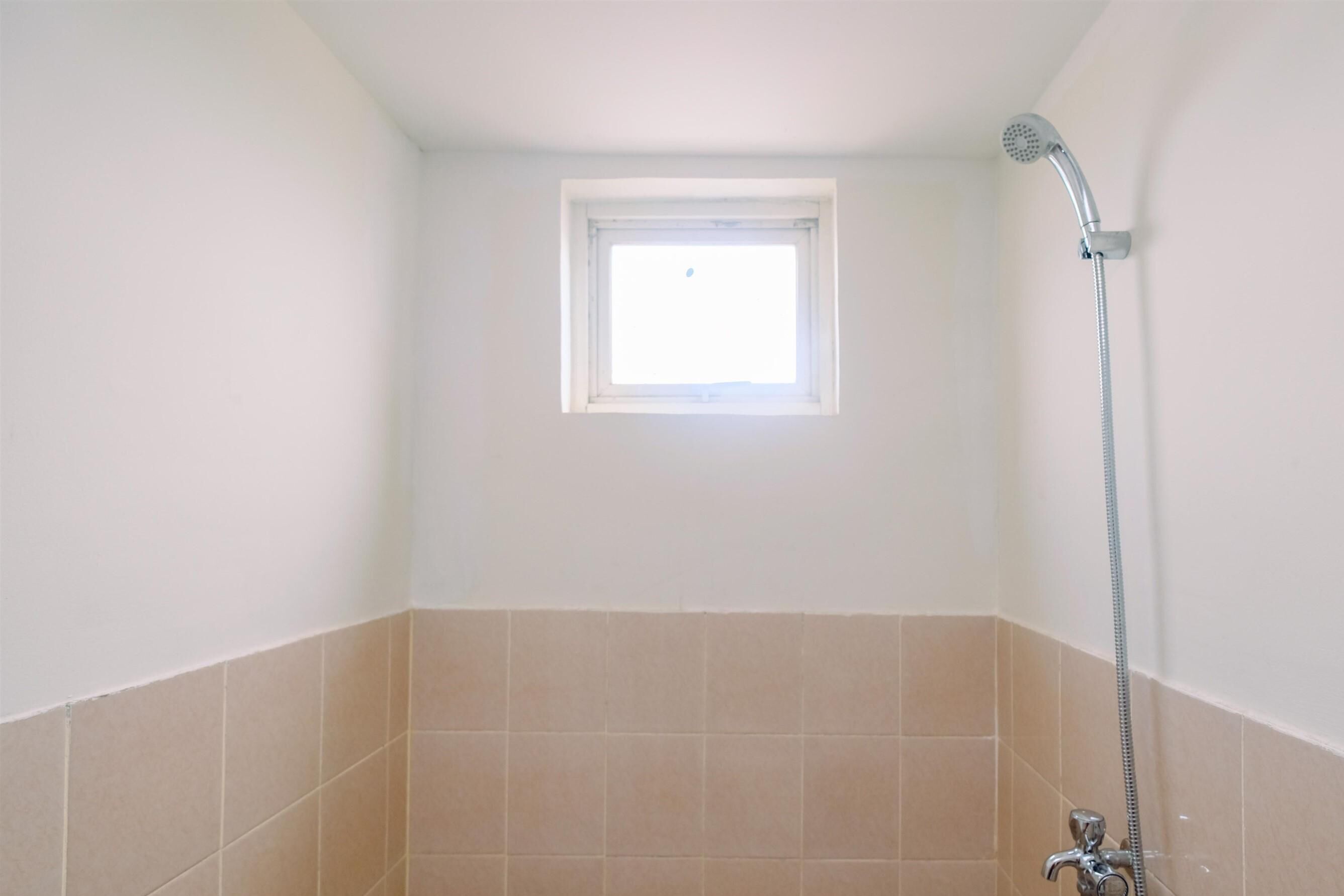 Ein kleines Badezimmer mit Dusche, Fenster und beigen Fliesen.
