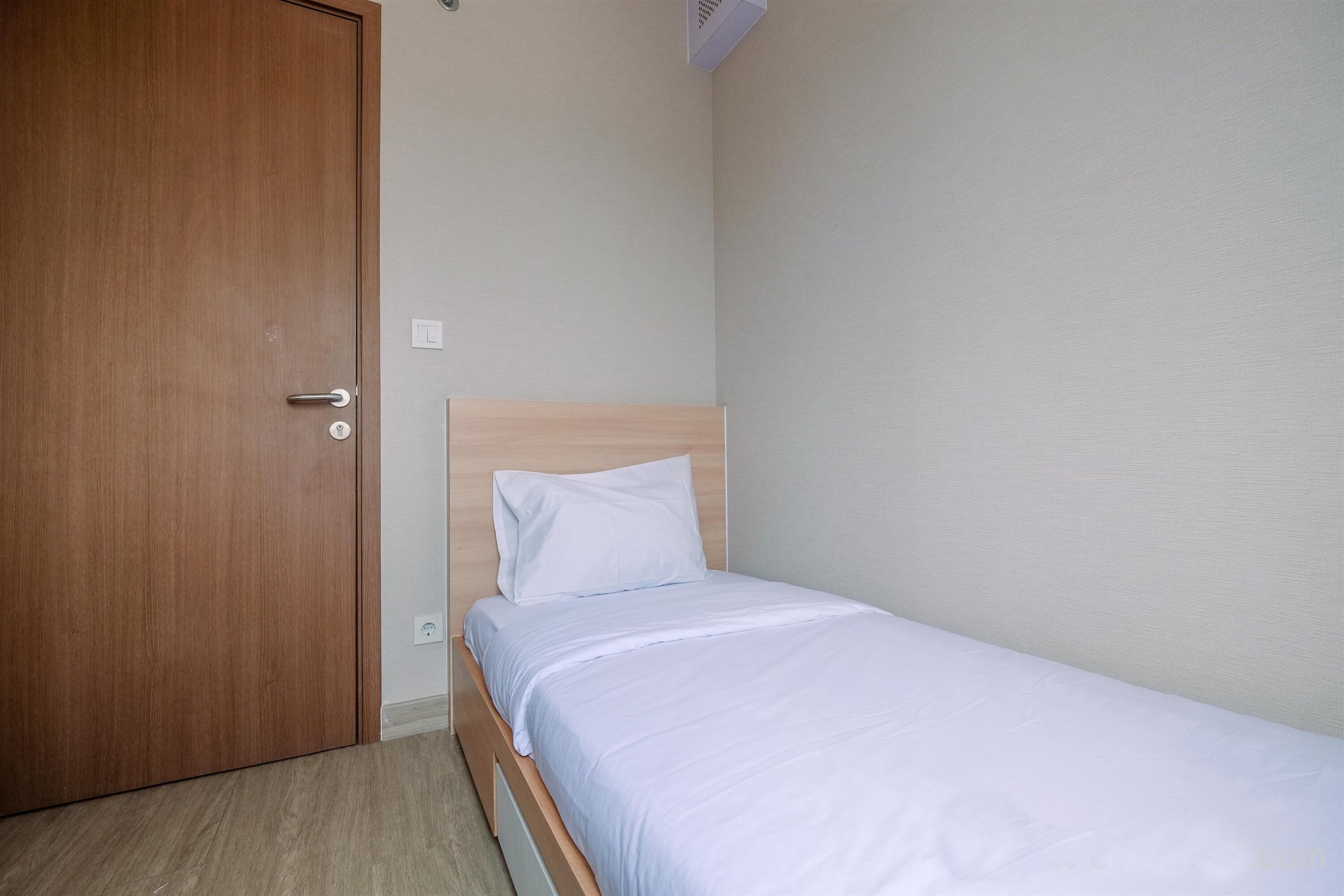 Un petit lit bien fait, avec une tête de lit en bois, dans une pièce dotée d’une porte en bois et de murs aux couleurs claires.