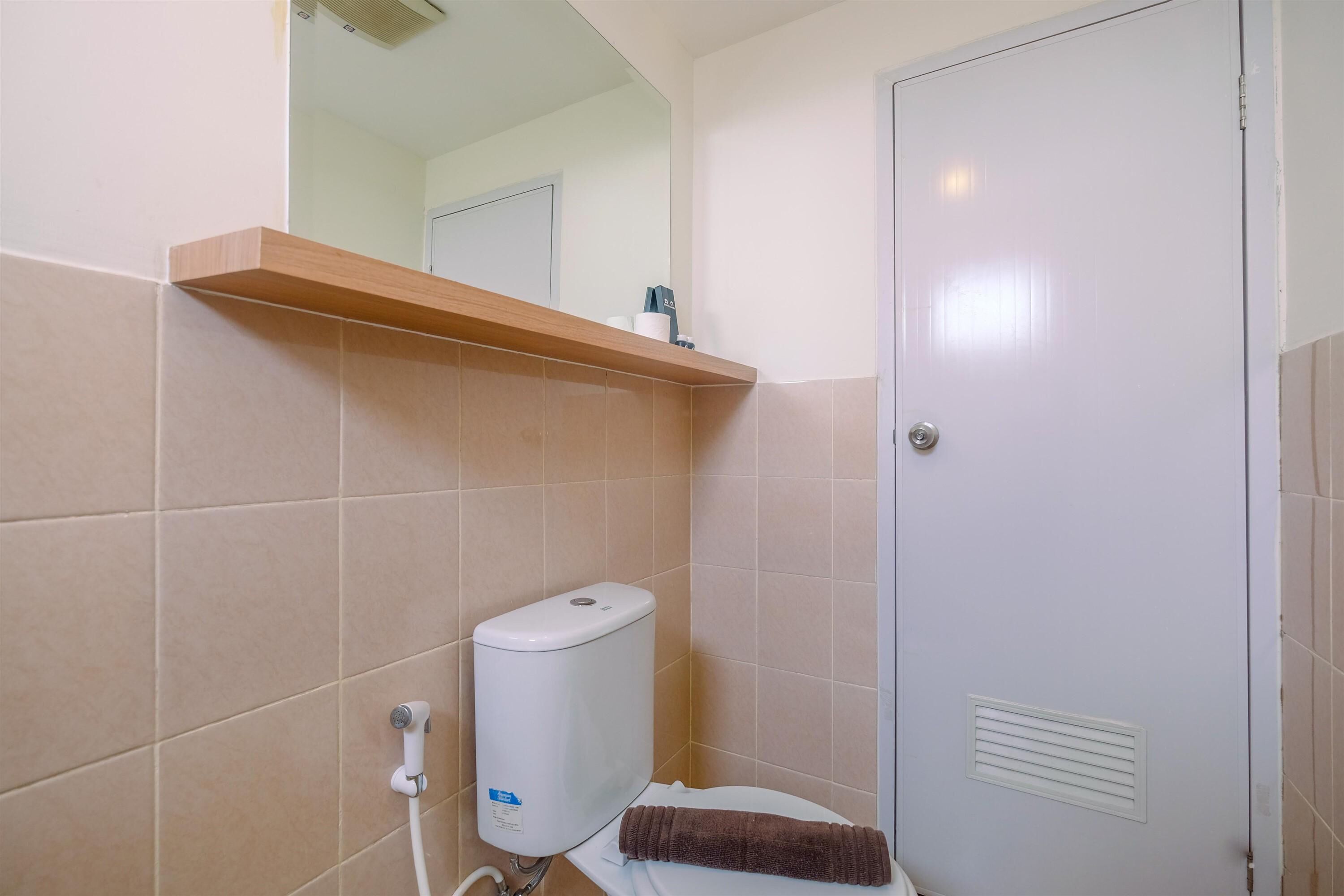 Ein Badezimmer mit beigen Fliesen, einer weißen Toilette, einem Handtuch, einem Seifenspender und einem Spiegel über dem Waschbecken.
