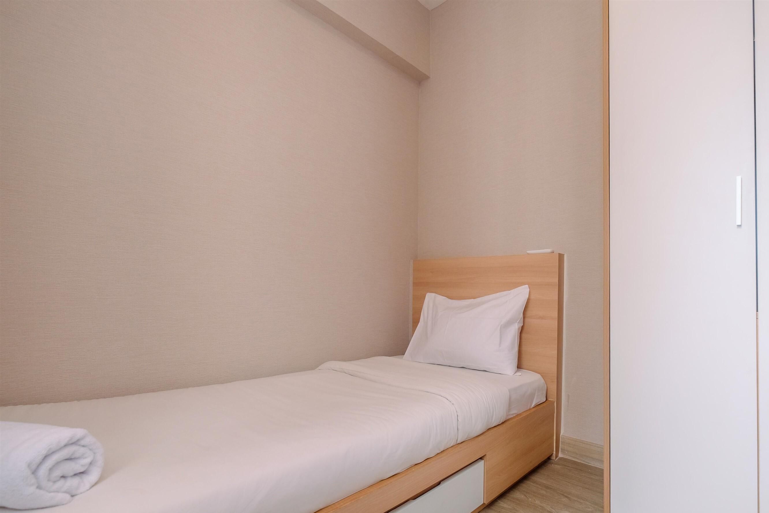 A small, single-bed room with a wooden headboard, a white mattress, and a neatly folded white towel on the bed.