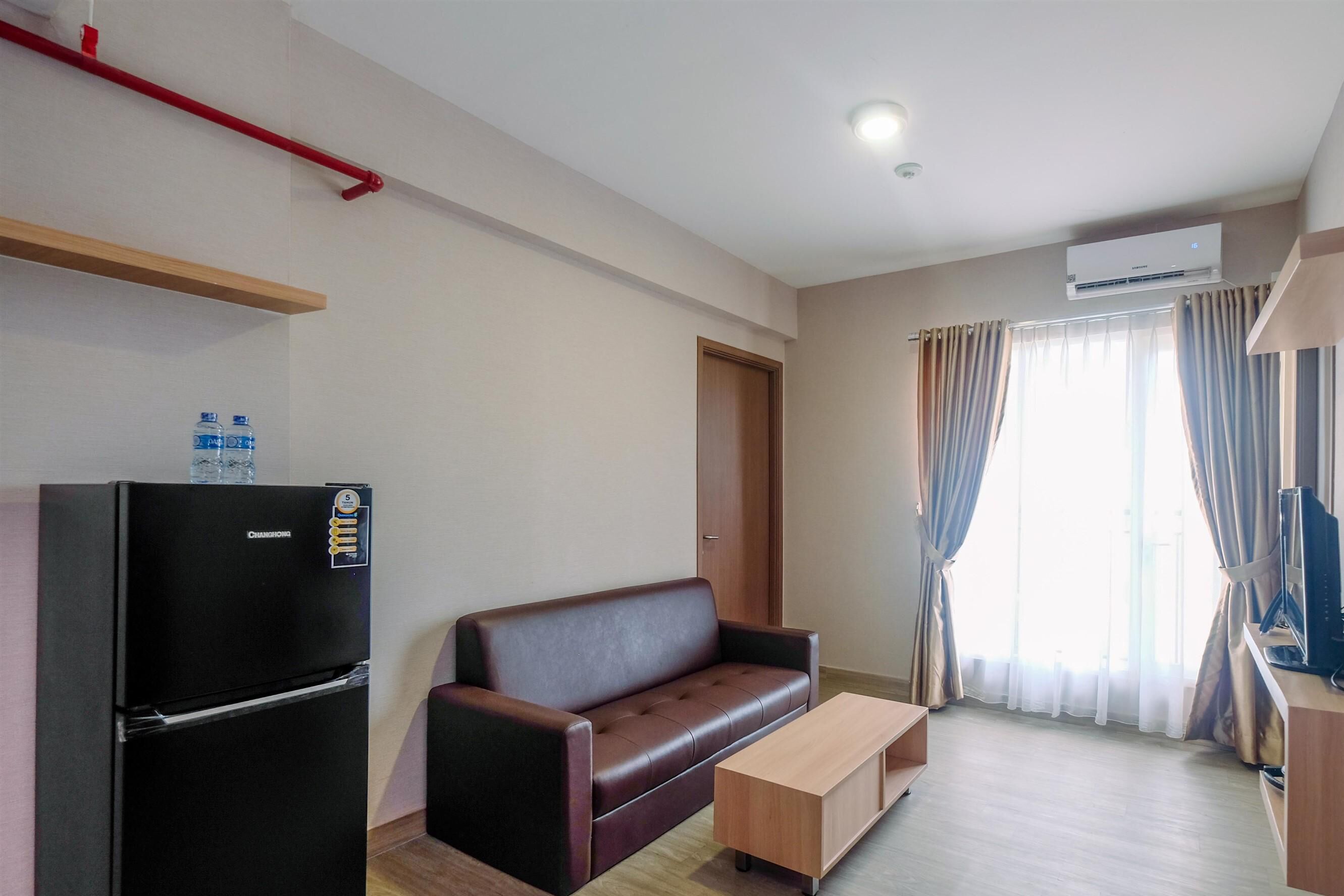 A compact living space with a sofa, a small table, a refrigerator, and a television.