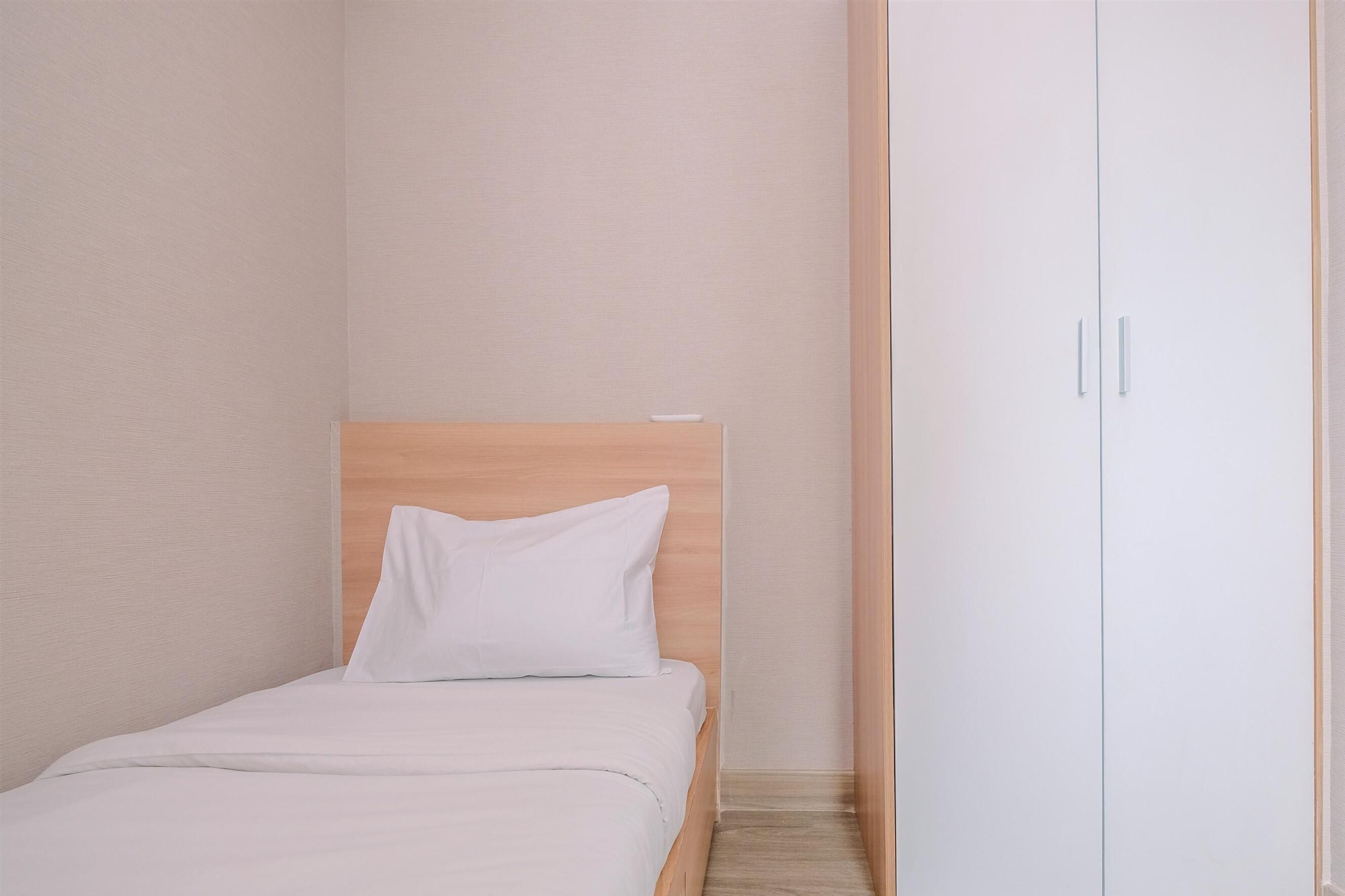 A bedroom with a wooden headboard, a single bed with white bedding, and a white wardrobe with two doors.