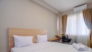 Ein Hotelzimmer mit hölzernem Kopfteil, einem Bett mit weißen Leinen, einem Schreibtisch mit Stuhl und einer Klimaanlage.