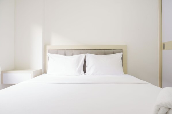 A neatly made bed with a wooden headboard and white bedding in a minimalist room.