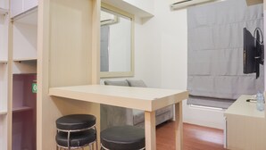 Ein kleiner, moderner Raum mit einem Holztisch, zwei schwarzen Hocker, einem grauen Sofa, einem großen Spiegel und einem grauen Vorhang.