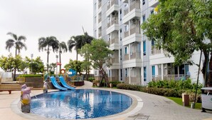 A swimming pool with slides, surrounded by a building with balconies and palm trees. - Homey and Simple Studio at Tanglin Supermall Mansion Apartment (Surabaya)