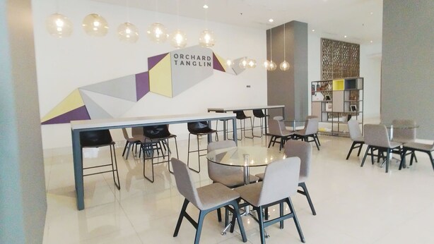 A modern dining area with a glass table and chairs, a sign reading "ORCHARD TANGLIN," and a decorative wall with geometric patterns. - Homey and Simple Studio at Tanglin Supermall Mansion Apartment (Surabaya)