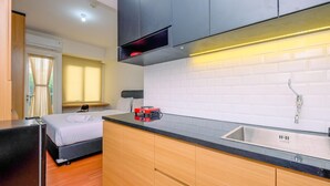 Une chambre d’hôtel compacte comprenant un coin cuisine, un lit près d’une fenêtre et une salle de bain avec des toilettes.