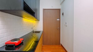 Une cuisine compacte dotée d’un plan de travail noir, d’une plaque de cuisson à induction rouge et d’un évier en acier inoxydable.