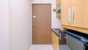 A narrow kitchen with a wooden door, a black dishwasher, and wooden cabinets. - Nice and Comfort Studio at 25th Floor Podomoro Golf View Apartment (Gunung Putri)