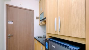 A compact kitchen with wooden cabinets, a black refrigerator, and a built-in microwave. - Nice and Comfort Studio at 25th Floor Podomoro Golf View Apartment (Gunung Putri)