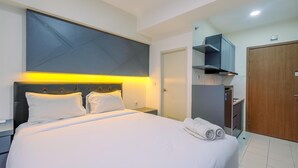 A modern hotel room with a large bed, a flat-screen TV, a wooden wardrobe, and a built-in desk. - Comfy and Homey Studio at Podomoro Golf View Apartment (Gunung Putri)