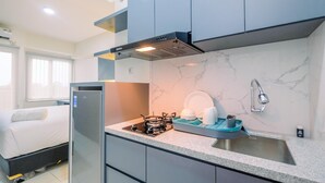 A compact kitchen with a built-in gas stove, a sink, and a compact refrigerator. - Comfy and Homey Studio at Podomoro Golf View Apartment (Gunung Putri)