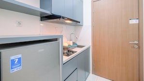 A compact kitchen with grey cabinets, a stainless steel refrigerator, and a wooden door. - Comfy and Homey Studio at Podomoro Golf View Apartment (Gunung Putri)