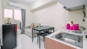 Una cocina compacta con comedor, refrigerador, lavamanos y ventana con cortinas.