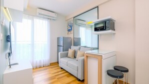 A compact living space with a kitchenette, a sofa, a dining table with two stools, and a large mirror.