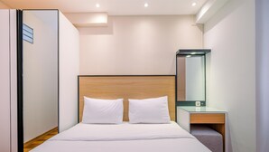 A modern hotel room with a wooden headboard, a bed with white linens, a bedside table, and a mirror.